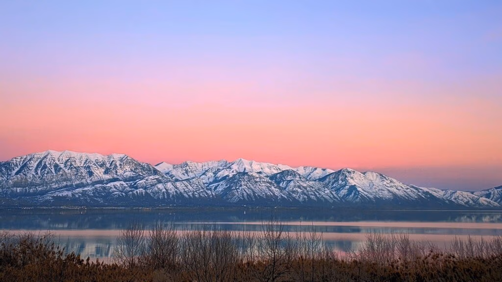 Snow-capped mountains at dawn with a pastel sky and serene lake, representing Wasatch County's natural beauty and community engagement.