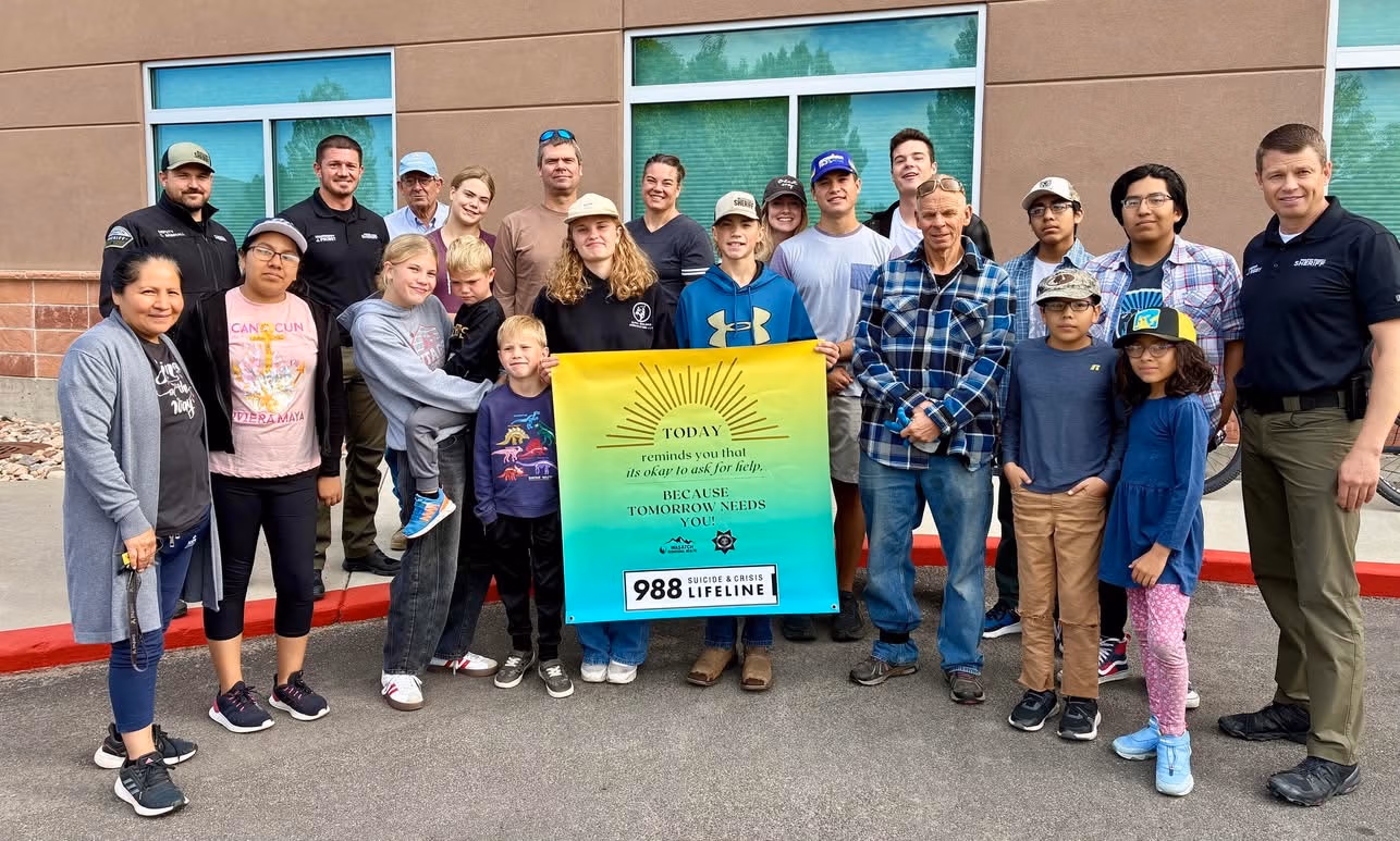 Community members and law enforcement officers in Wasatch County gathered for a group photo, holding a banner promoting mental health awareness and resources, emphasizing local engagement and support initiatives.