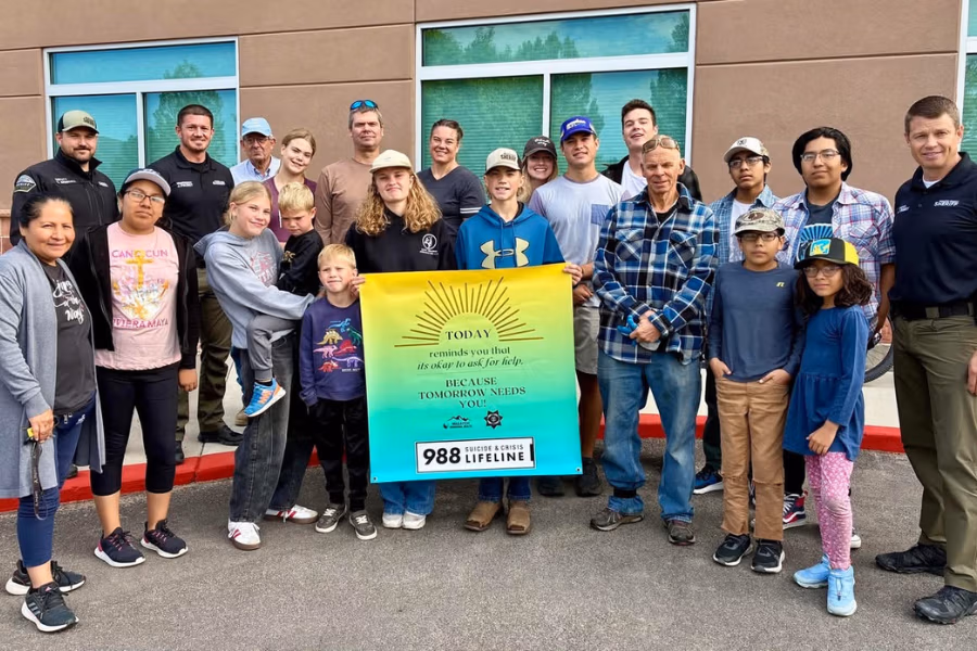 Group of community members and law enforcement officers in Wasatch County holding a sign promoting mental health awareness with the text "Today reminds us that it’s okay to ask for help because tomorrow needs you," emphasizing community safety and support initiatives.