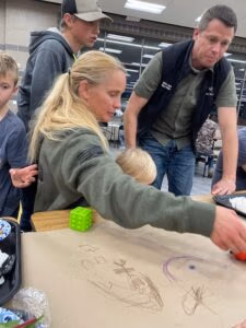 Family engaging in community activity, drawing on paper, with children and adults participating, highlighting community involvement and support initiatives in Wasatch County.