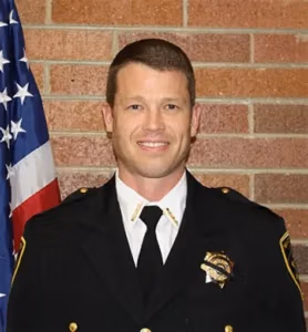 Sheriff Jared Rigby in uniform, smiling, with an American flag in the background, representing modernized law enforcement in Wasatch County.