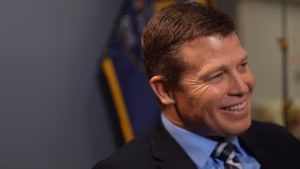 Smiling man in a suit, representing Sheriff Jared Rigby, with a background indicating law enforcement context, emphasizing community connection and safety initiatives.